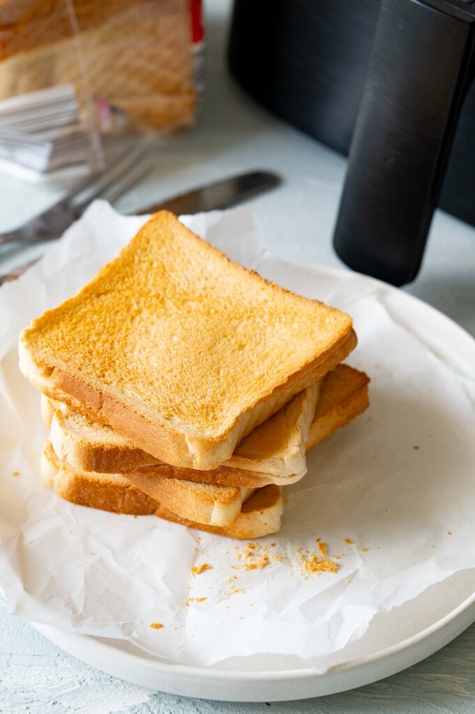 Vier Scheiben getoasteter Toast auf einem Teller gestapelt. Im Hintergrund ist ein Airfryer zu sehen.