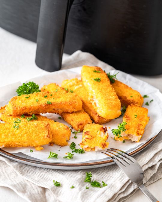 Fischstäbchen TK in der Heißluftfritteuse gebacken auf einem Teller mit Petersilie.