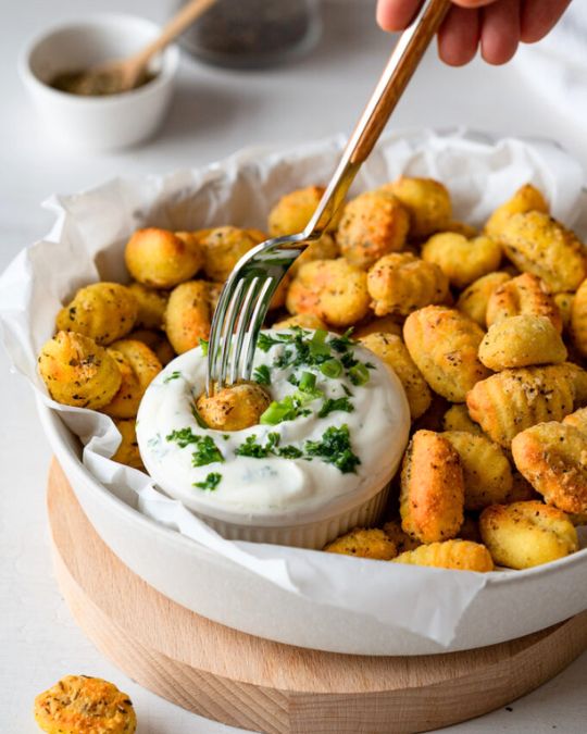 Knusprige Gnocchi aus der Heißluftfritteuse. Ein Gnocchi wird gerade mit einer Gabel in einen Kräuterquark gedippt.