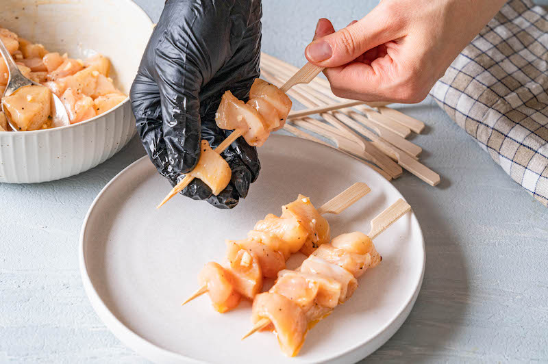 Die Hähnchenfleisch-Stücke werden auf Spieße gesteckt.