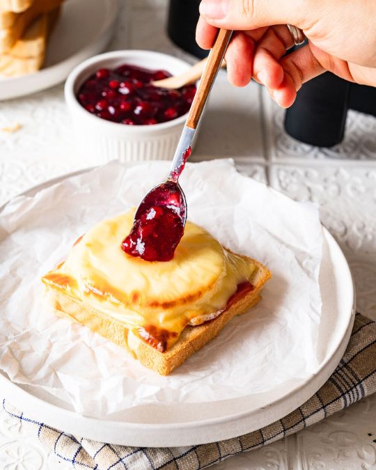 Toast Hawaii aus der Heißluftfritteuse wird gerade mit Preiselbeeren verziert.